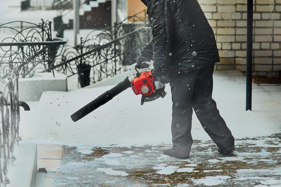 Benzínový fukár pri čistení chodníka od napadaného snehu.